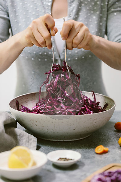 A woman is photographed as she is mixing a red cabbage salad